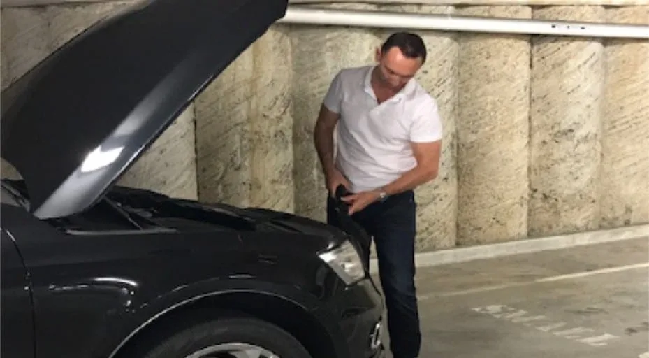 Technician inspecting under the bonnet of a dark sedan for tracking devices